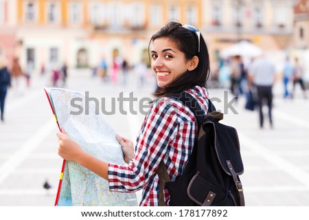 Kind tourist with backpack smiling and examining map.