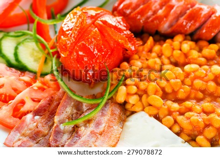 A closeup of continental breakfast containing sausages, bean truck, bacon, fresh vegetables, fried eggs and bread.