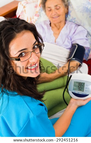 Doctor measuring blood pressure in nursing home with digital device.