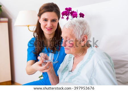 Caring nurse helping sick elderly woman to drink in bed in a nursing home.
