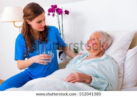 Kind geriatric doctor bringing water to the senior woman in need.