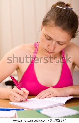 A young woman studying at the desk with a serious facial expression.
