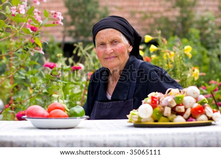 An elderly woman sitting at the table with healthy food in front of her in old vessels.