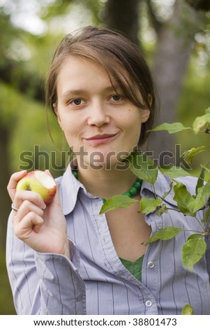 A beautiful young woman in casual clothing eating a fresh red apple outdoors.