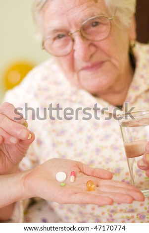 A young doctor giving medications - drugs and vitamins - and a glass of fresh water to an elderly woman - focus on pills.