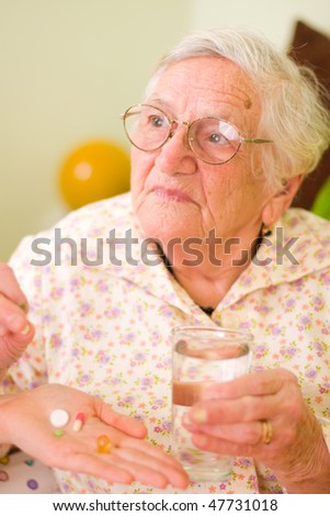A young doctor giving medications - drugs and vitamins - and a glass of fresh water to an elderly woman.