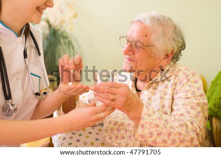 A young doctor giving medications - drugs and vitamins - and a glass of fresh water to an elderly woman.