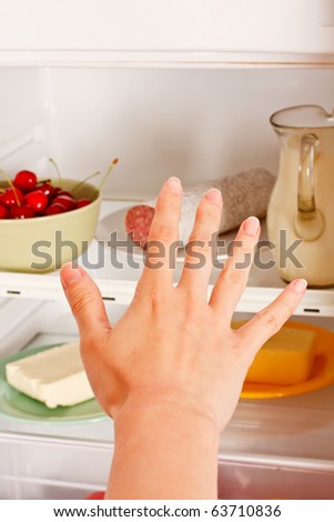A young woman\'s hand reaching out for food from the refrigerator.