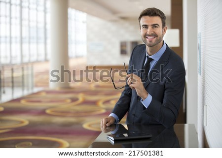 Happy businessman with glasses using tablet at the hotel lobby