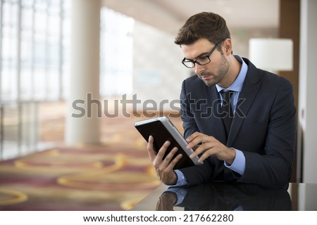 Focused businessman with glasses using smart electronic tablet at the hotel airport lobby checking stock market report