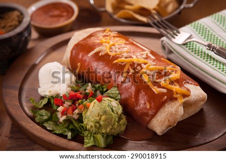 Large restaurant style burrito mexican food dinner with sides of guacamole chips