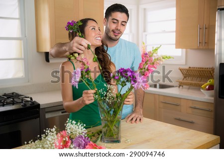 Playful man and woman dating put flowers into a vase at home in the kitchen
