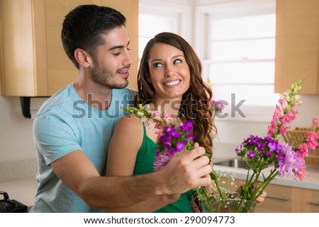 Two young lovers laugh and play in happiness lovingly putting flowers from their garden into a vase