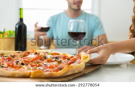 Close up of supreme pizza slice and people eating and enjoying wine at home delivery