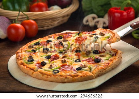 Delicious cheese stringy slice lifted of full supreme pizza baked fresh out of the oven next to ingredients