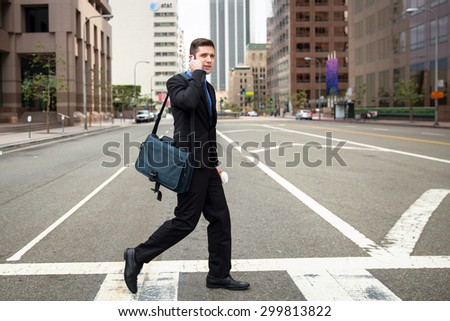Businessman crossing the street crosswalk on way to work fast paced with cellphone