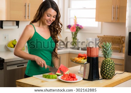Beautiful woman home in kitchen making a smoothie with blender fresh fruit ingredients organic