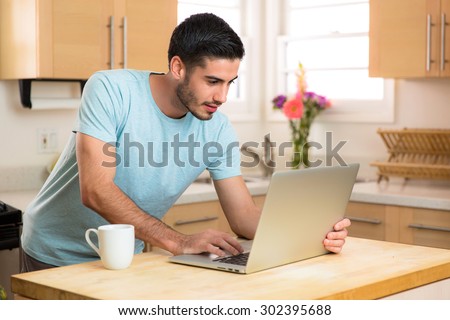 Man reads news on internet laptop computer in the morning with coffee at home bright sunny day