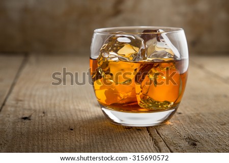 Glass of scotch whisky brandy with ice on wooden bar table rustic barrel surface