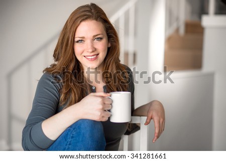 Beautiful female relaxed with cup of tea coffee indoor blonde head shot space modern interior living staircase