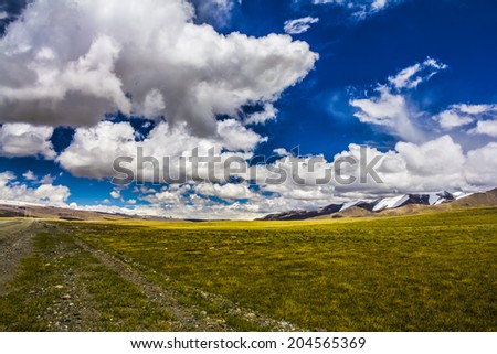 Panoramic view of high mountains. Meadow with green grass under blue sky with light clouds