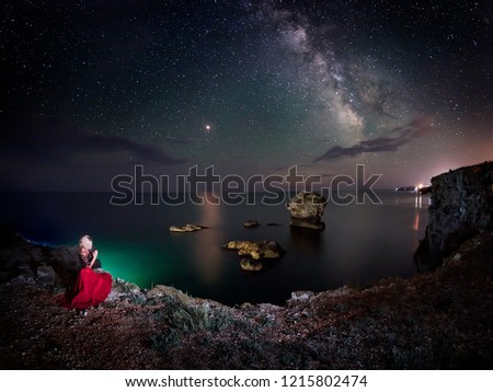 young woman and stunning vibrant Milky Way image over rocky cliffs and sea, night landscape
