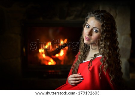 beautiful woman with red cloak sitting by the fire