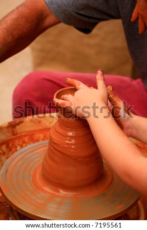 A potters hands guiding a child hands to help him to work with the ceramic wheel