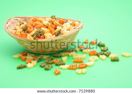 small basket with assorted colorful uncooked pasta on green background