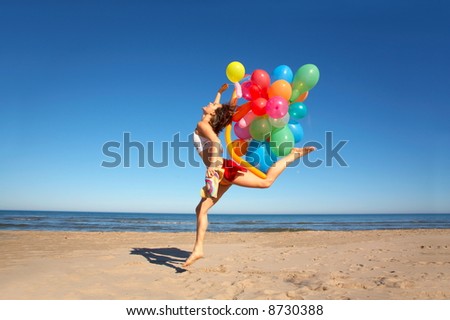 happy young woman jumping on the beach with different colored balloons