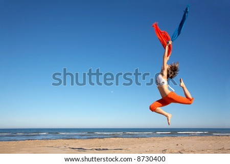 happy young woman jumping on the beach with different colored scarves