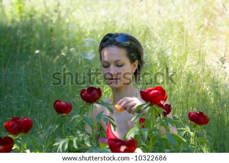 teen girl on a field with green grass and red peonies blowing soap balloons