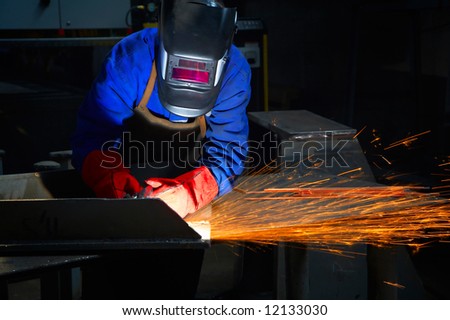 worker with protective mask and gloves grinding/welding metal and sparks spreading