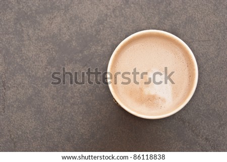 a cup of hot coffee in paper cup taken from the top view with creamy milk inside