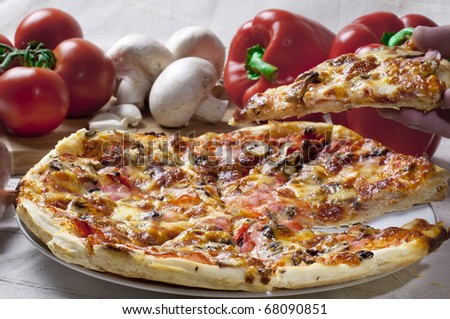 Pizza with ingredients on the table a slice is lifted with the hand