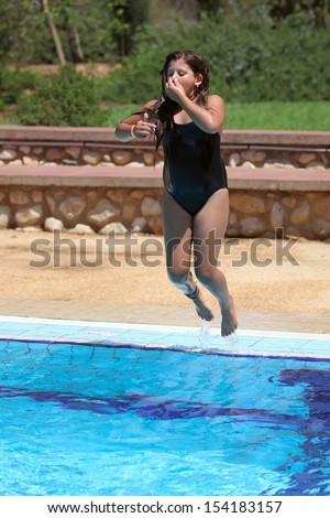 Girl jumping in swimming pool holding her nose