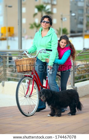 a mother, a daughter and a dog with a bike on the street