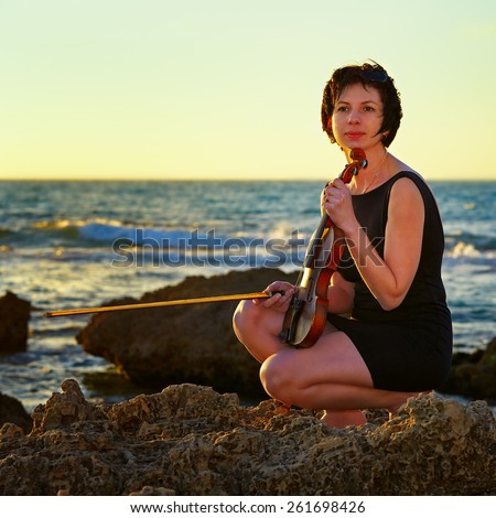 a young beautiful brunette woman music lover on beach with a violin at sunset