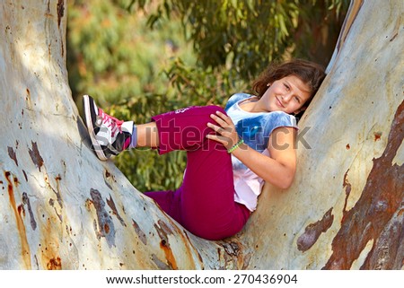 school aged girl climbed on tree and sitting on tree branch