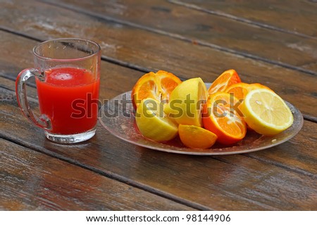 A fruit plate of oranges and lemons on a wet wooden table after rain, and a glass of fresh red juice.