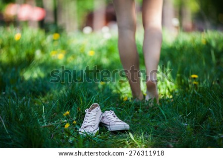 Woman walking barefoot on the grass, pink shoes in focus, shallow DOF