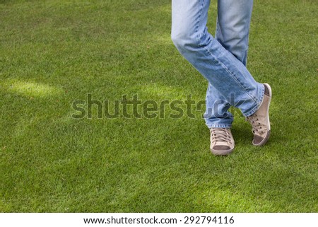 Crossed male legs on green grass field