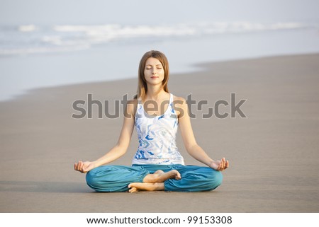 Young beautiful woman sitting in meditation pose on the beach