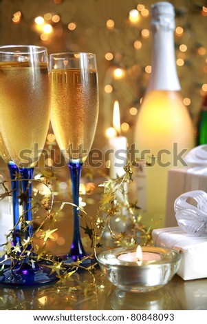 Champagne in glasses,bottle,gifts,candle lights and twinkle lights on gold background.