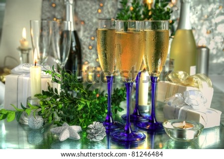Champagne in glasses,bottles,gifts,candle light and green twig on silver background.