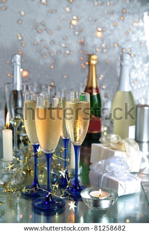 Champagne in glasses,bottles,gift boxes,candle light and twinkle lights on silver background.