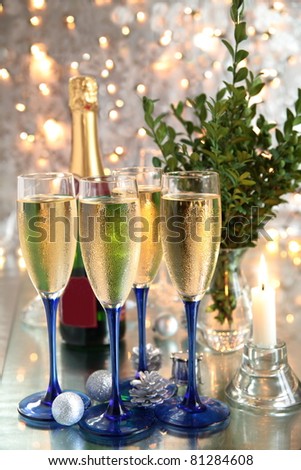 Champagne in glasses, bottle,candle light, green twig and twinkle lights on background.