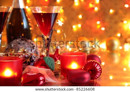 Closeup of bauble, candle lights  and red wine in glasses on gold background with lights.