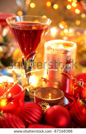 Closeup of glass with red wine and baubles,candle lights on gold background with twinkle lights.