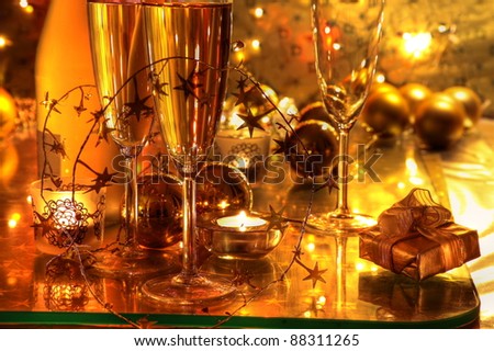 Closeup of champagne in glasses, gift box, candle lights on golden background.